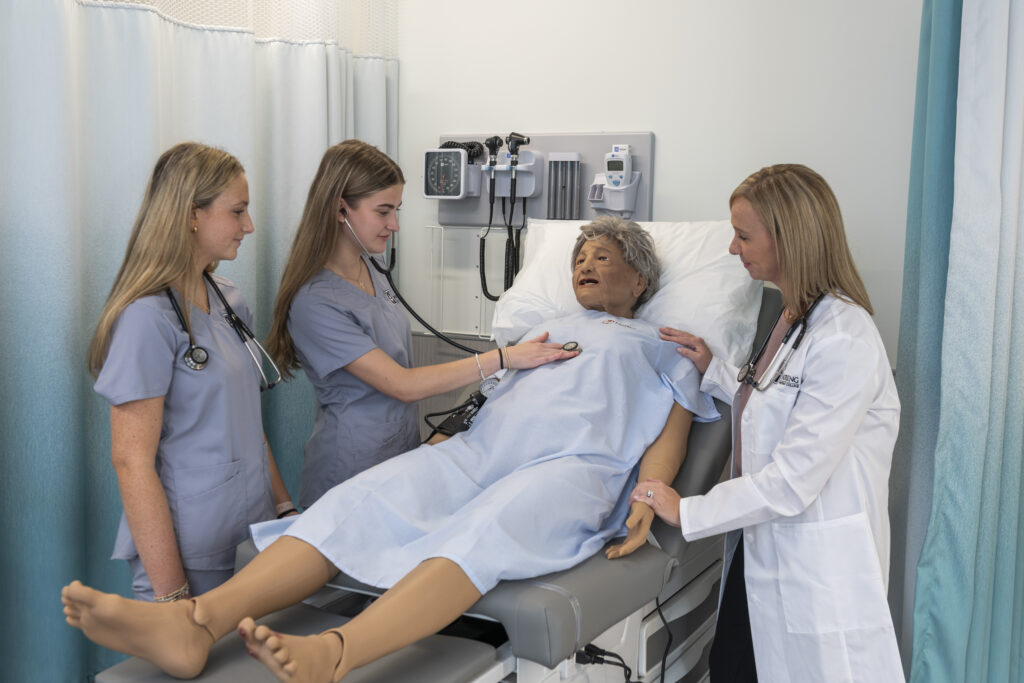 Nursing faculty with students using stethoscope on a medical manikin. 